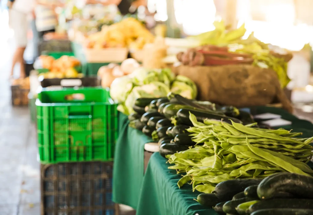 Display of fresh organic vegetables at a local market with green crates and produce on tables